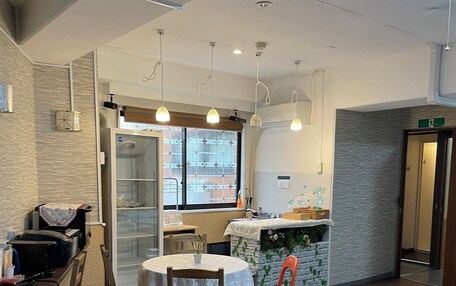 A hotel room with a bed, a dining table, chairs, a kitchen area, and a view through a window.