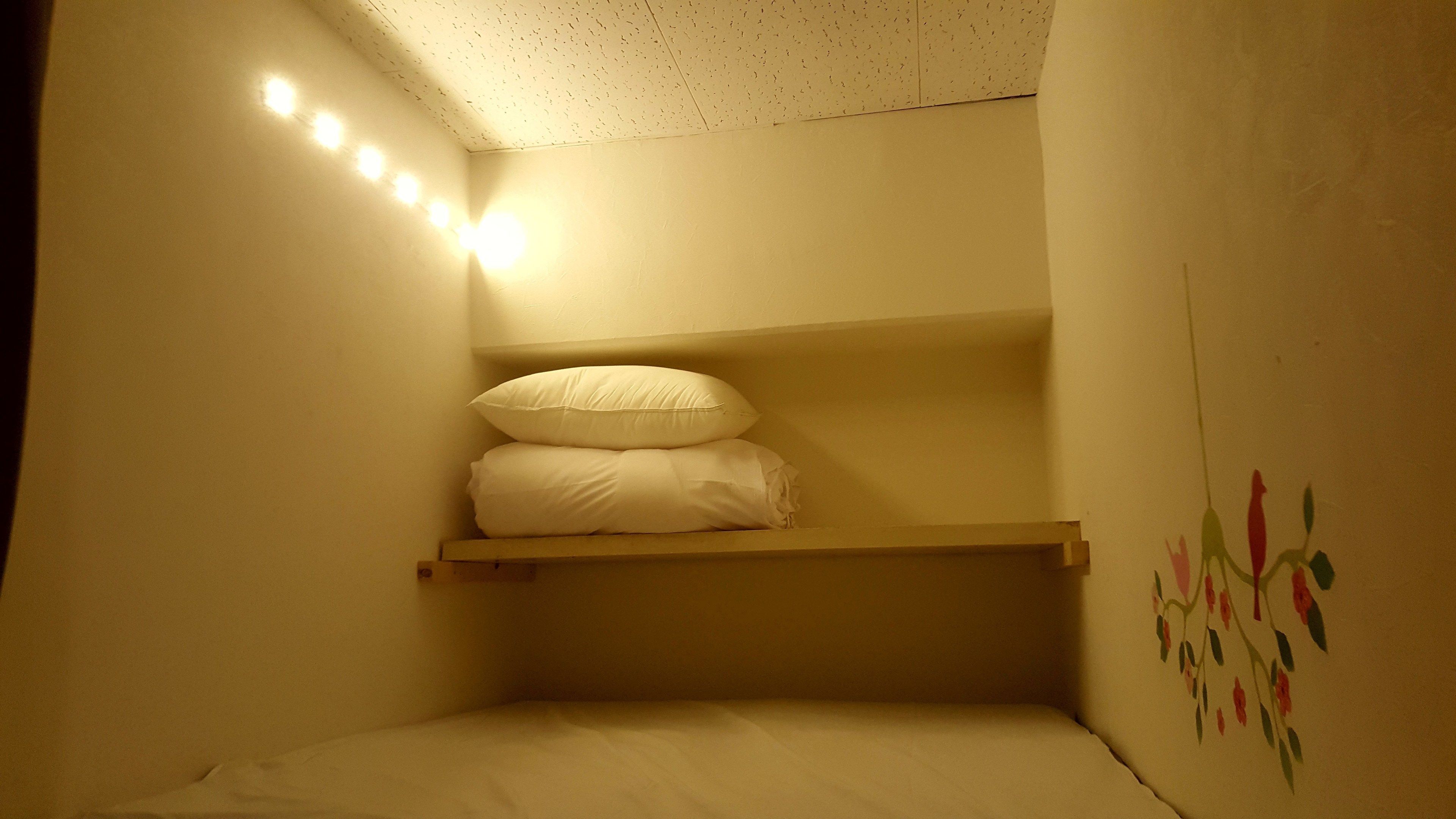 Una habitación pequeña y tenuemente iluminada con una litera, un estante con almohadas y un adorno en la pared.