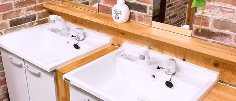 A bathroom with two white sinks, a wooden vanity, a mirror, and a brick wall.