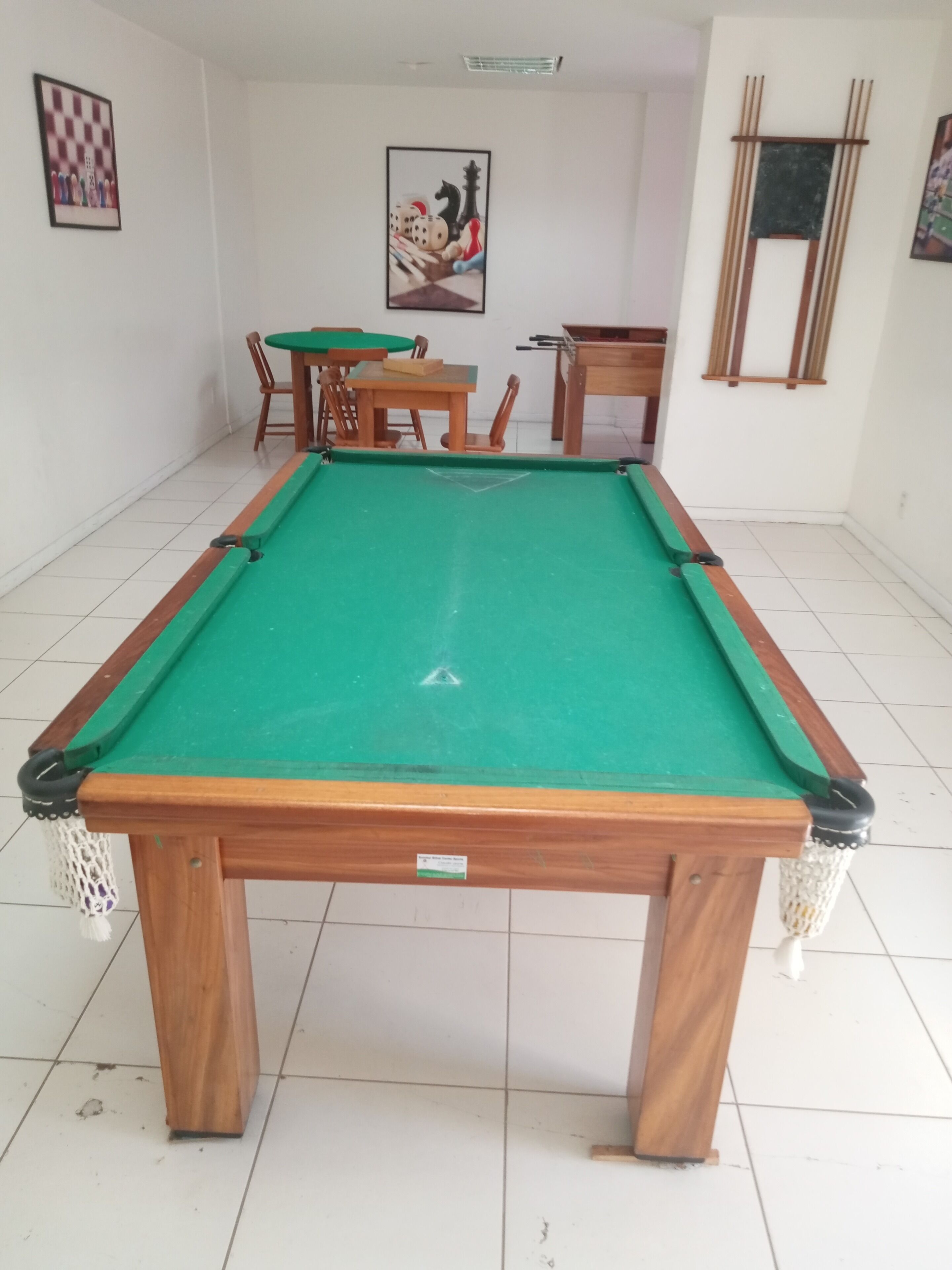 A pool table with a green felt surface, surrounded by wooden chairs and a small table.