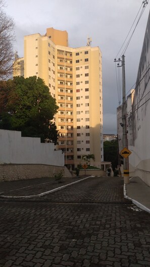 A tall residential building with multiple balconies and a paved street in front.