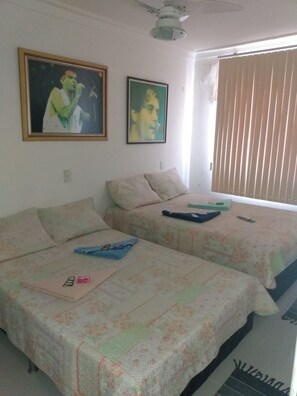 A room with two beds, a ceiling fan, and two framed pictures on the wall.