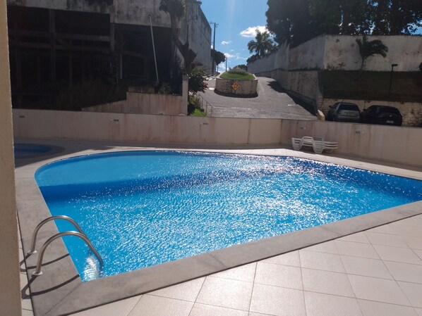 A swimming pool with a metal ladder, surrounded by a tiled deck.
