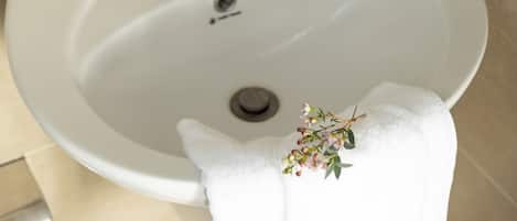 A bathroom with a white sink, a mirror above it, and a shelf with toiletries including a bottle of shampoo and a bottle of shower gel.