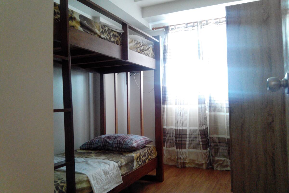A bunk bed room with a wooden floor, a door, and a window with curtains.