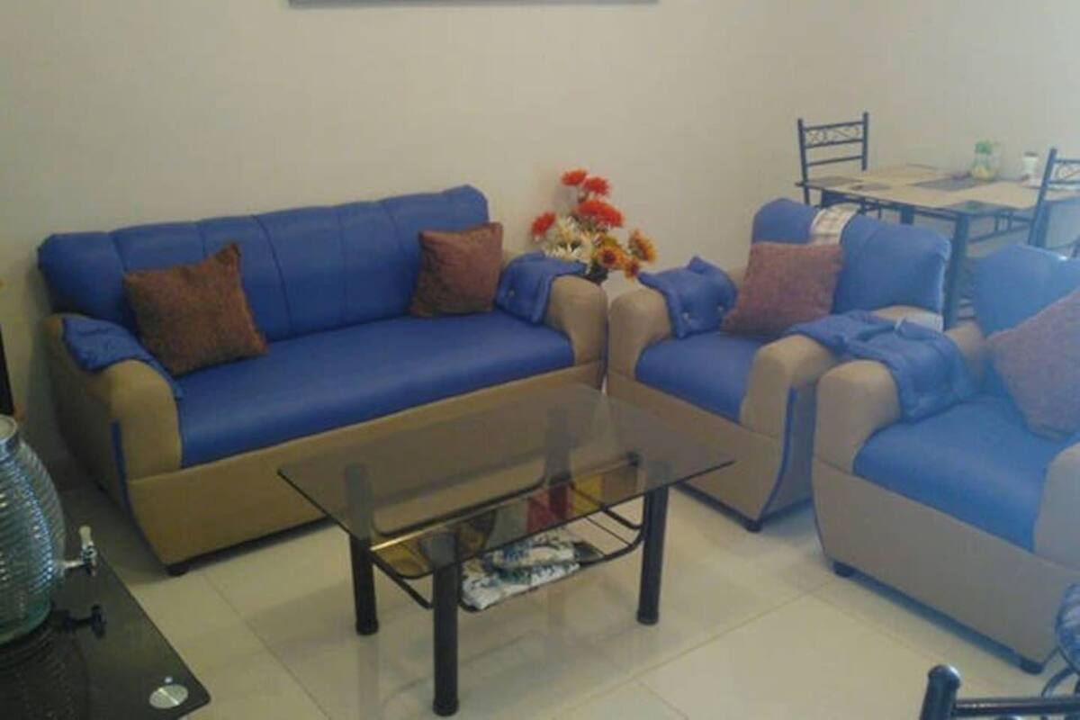 A living room with a blue sofa set, a glass coffee table, and a dining table with chairs.