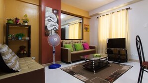A living room with a sofa, a coffee table, a TV, and a fan. - Camella Northpoint Condominium by Diamond Star Management Services (Davao)