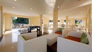 A spacious lobby with white wicker furniture, a foosball table, and large windows offering views of the outdoors. - Camella Northpoint Condominium by Diamond Star Management Services (Davao)
