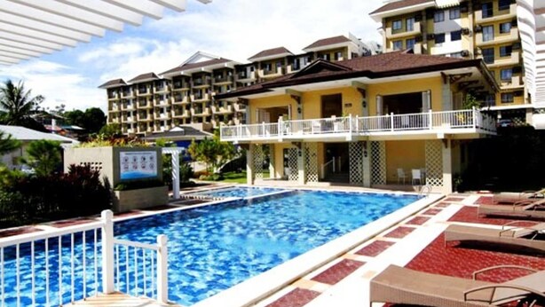 A swimming pool with a white deck and lounge chairs, surrounded by multi-story buildings with balconies. - Camella Northpoint Condominium by Diamond Star Management Services (Davao)