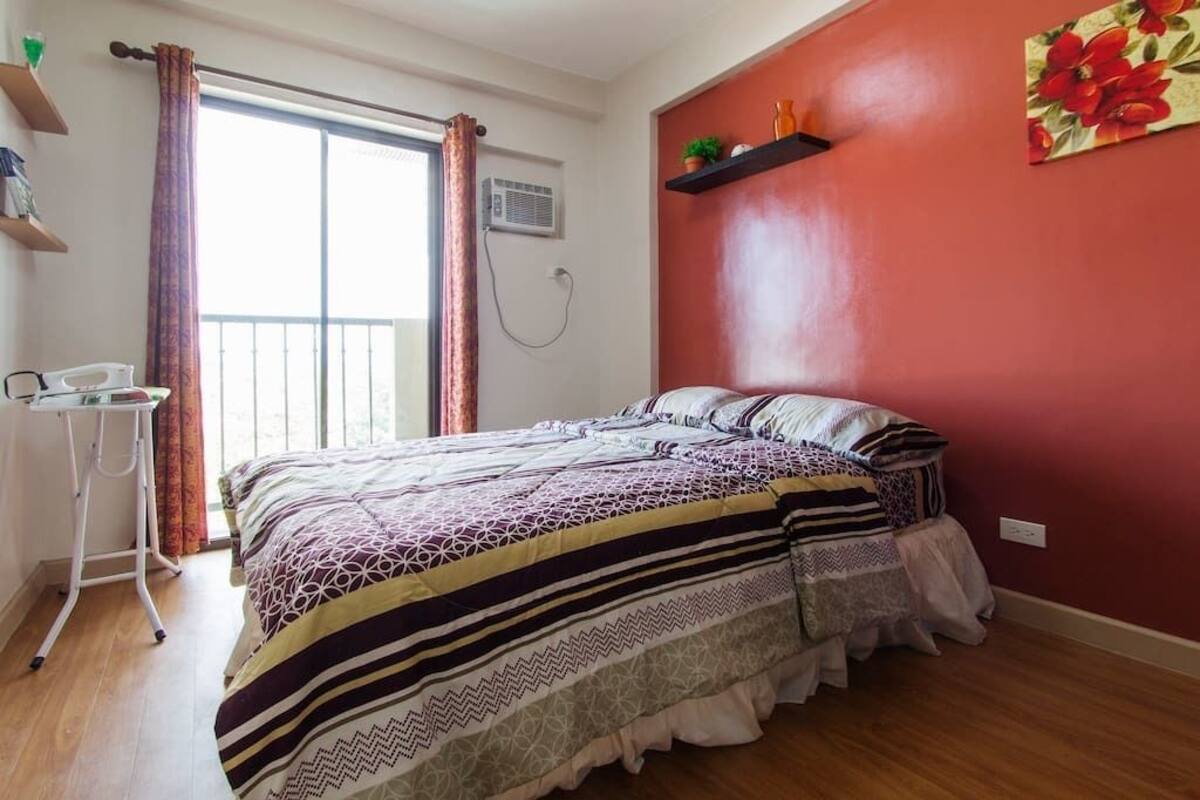 A bedroom with a bed, a desk, and a window with curtains.
