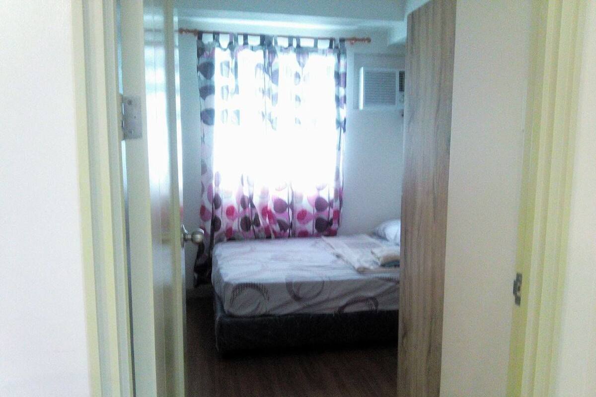 A small bedroom with a single bed, a window with curtains, and a door.