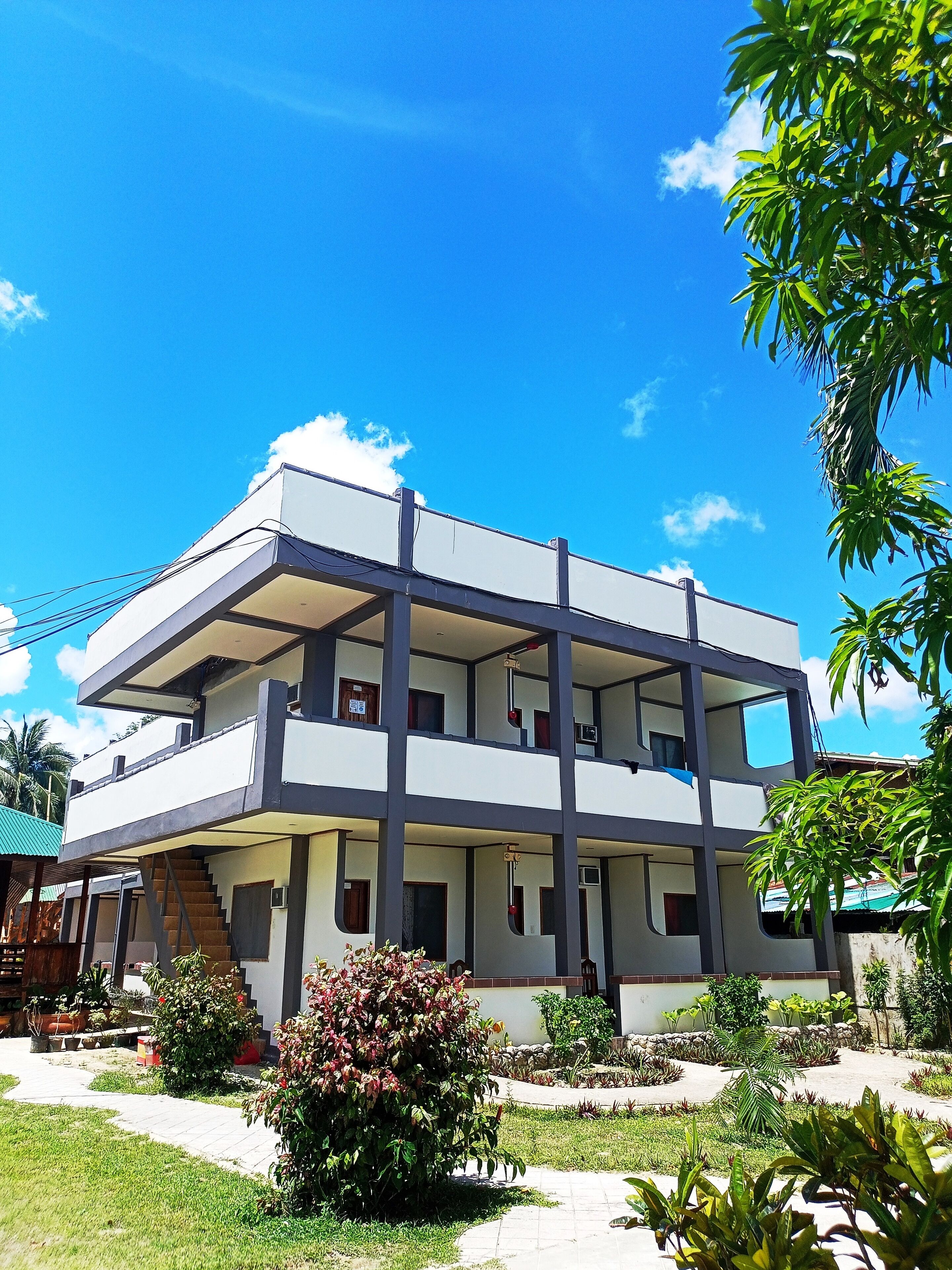A multi-story building with a flat roof, multiple balconies, and a garden area with various plants.