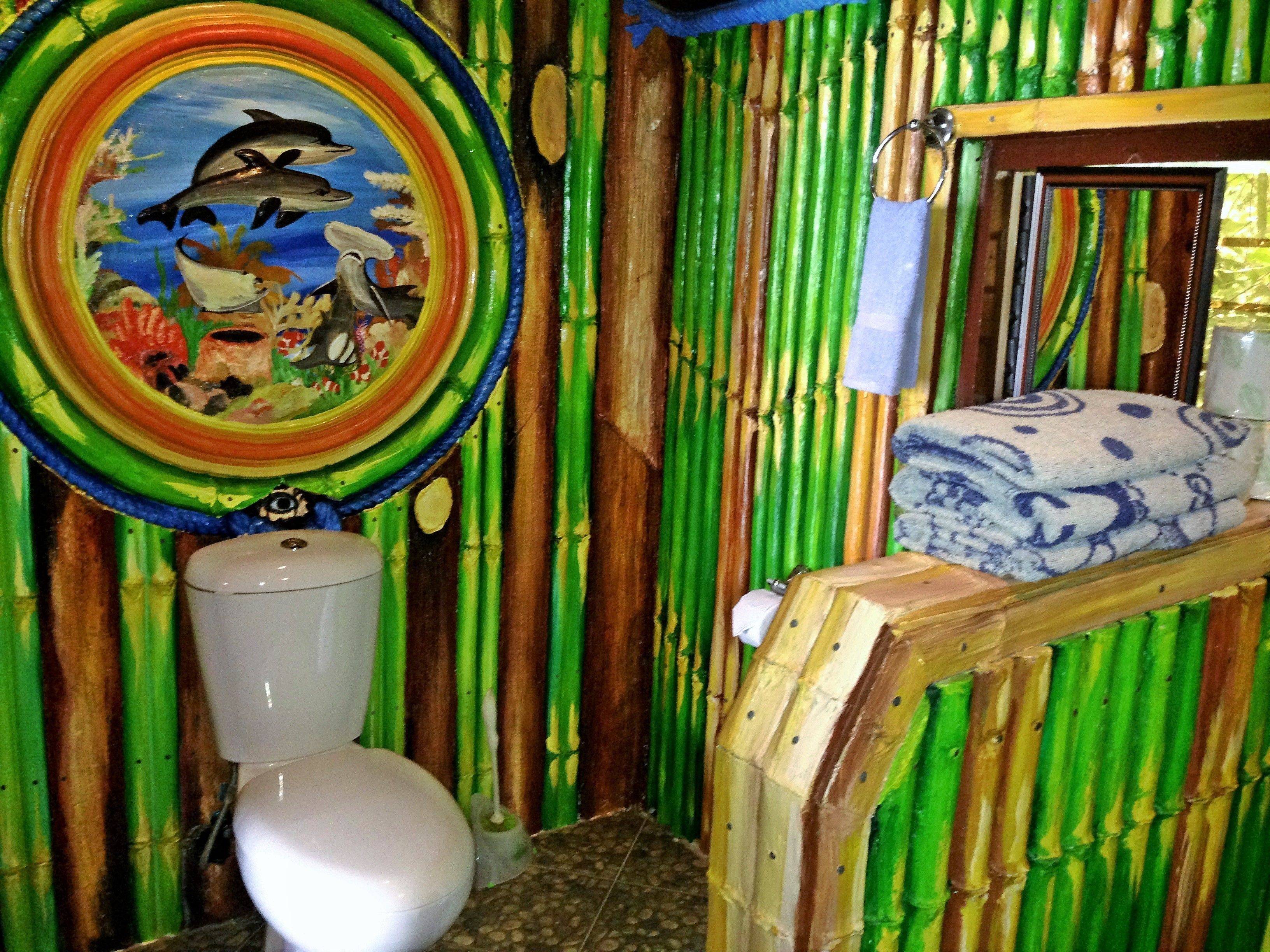 A bathroom with a toilet, a sink, and a mirror. The walls are covered with bamboo panels.