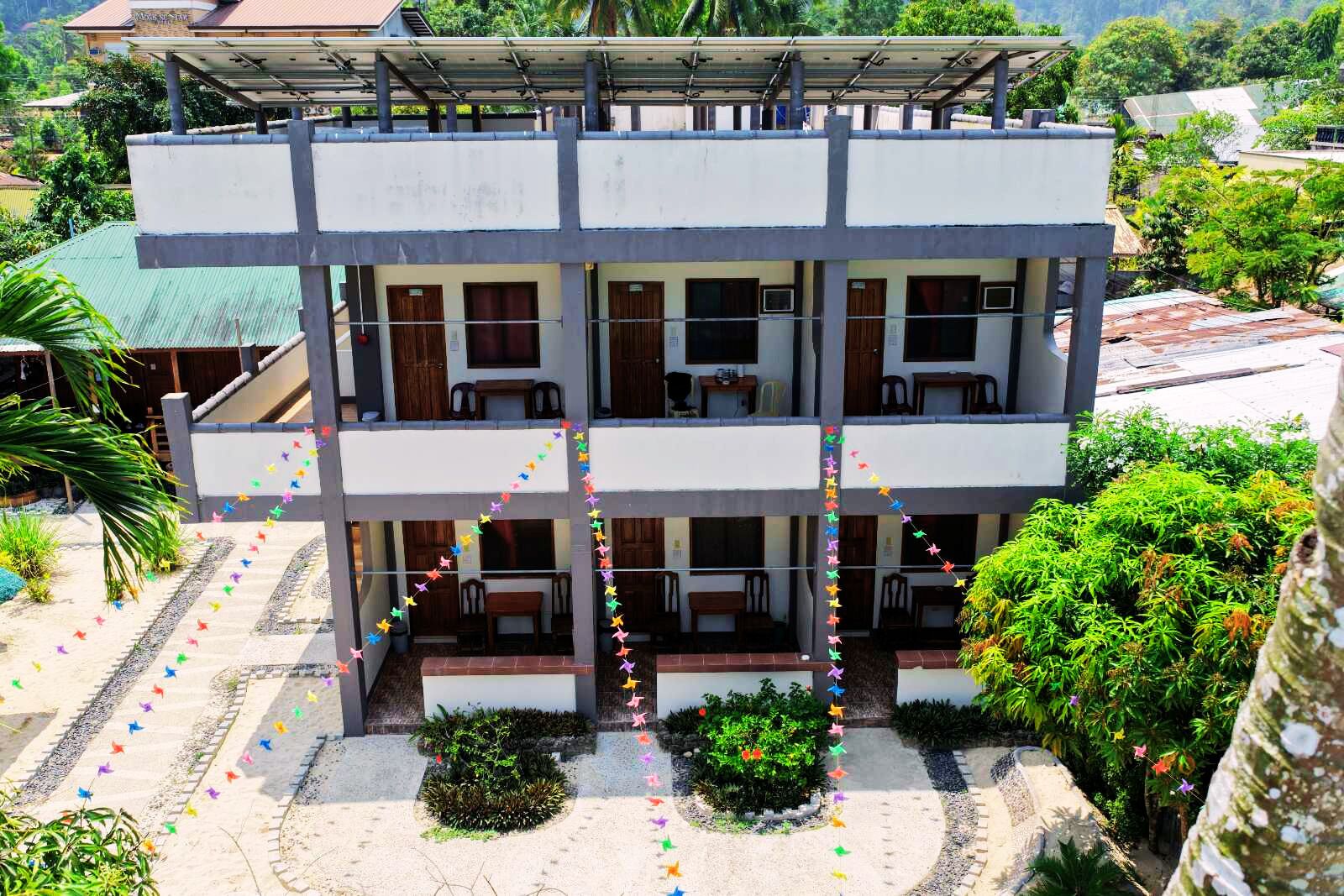 Un edificio de varios pisos con balcones, un espacio al aire libre cubierto y un jardín con plantas.
