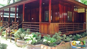 Een houten gebouw met een overdekte veranda, omringd door potplanten en palmbomen.