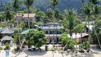 Un hotel frente al mar con varios pisos, palmeras y una playa de arena.