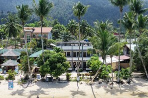 Un hotel frente al mar con varios pisos, palmeras y una playa de arena.