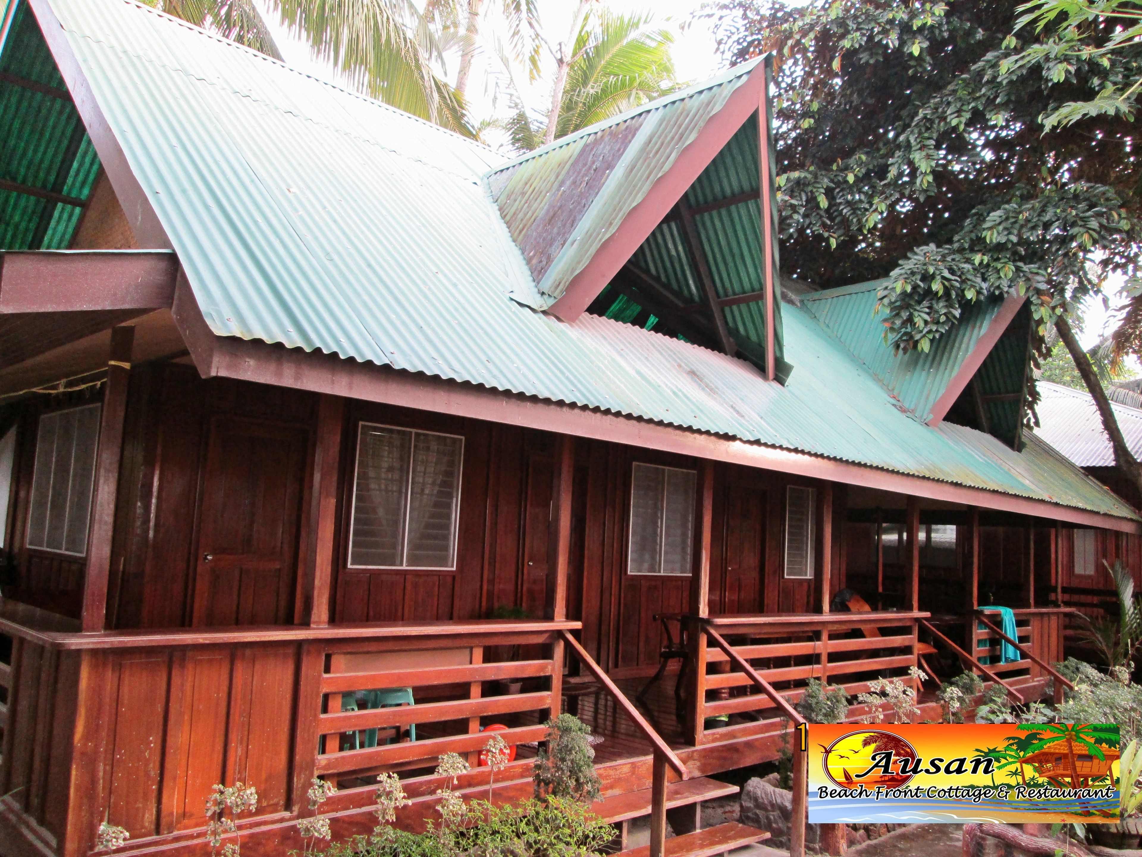 A wooden cottage with a corrugated metal roof, wooden stairs, and a porch.