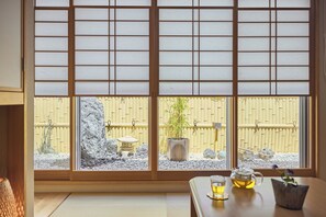 A traditional Japanese room with tatami flooring, a low table with a teapot and cup, and a view through shoji screens to a garden with a bamboo plant and a stone lantern. - KEYAKIAN Tokyo Nihonbashi (Tokyo)