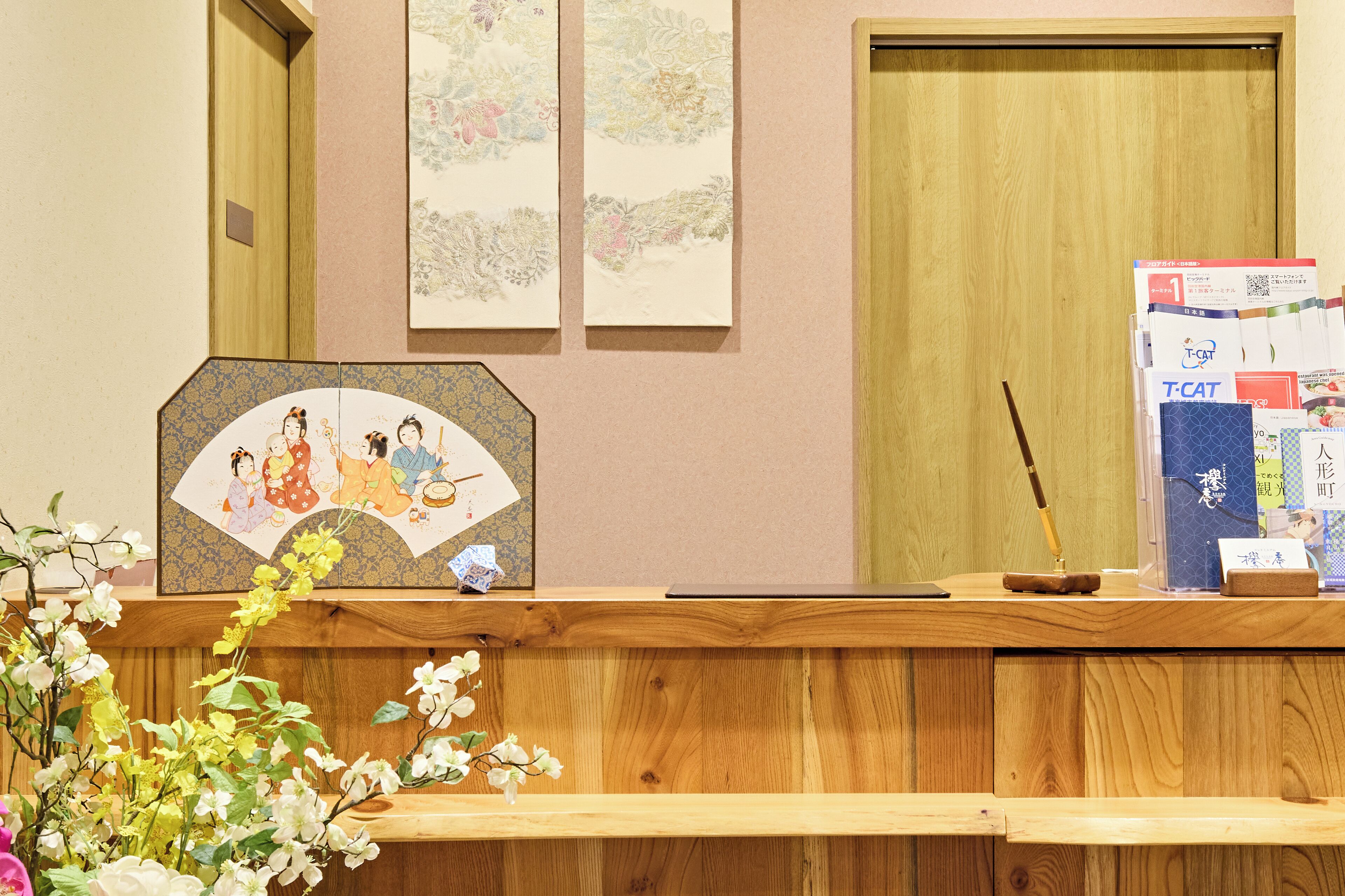 A reception desk with a traditional Japanese fan, a wooden door, and a wall with framed artwork.