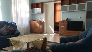A living room with a sofa, a coffee table, and a TV. There is a wooden cabinet and a small table with a clock. - Heart of Riga Apartment (Riga)