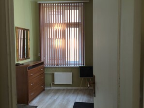 A room with a wooden dresser, a radiator, a small easel, and a window with vertical blinds.