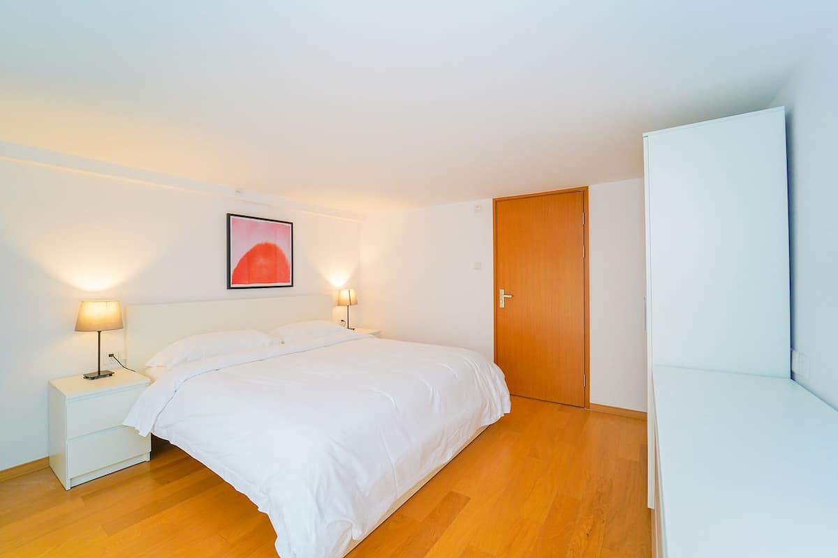 A bedroom with a bed, bedside lamps, a wooden door, and a white wardrobe.