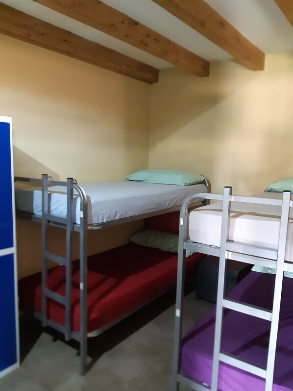 A dormitory room with bunk beds, wooden beams on the ceiling, and a blue wall. - A Cien Leguas - Hostel (Castrojeriz)