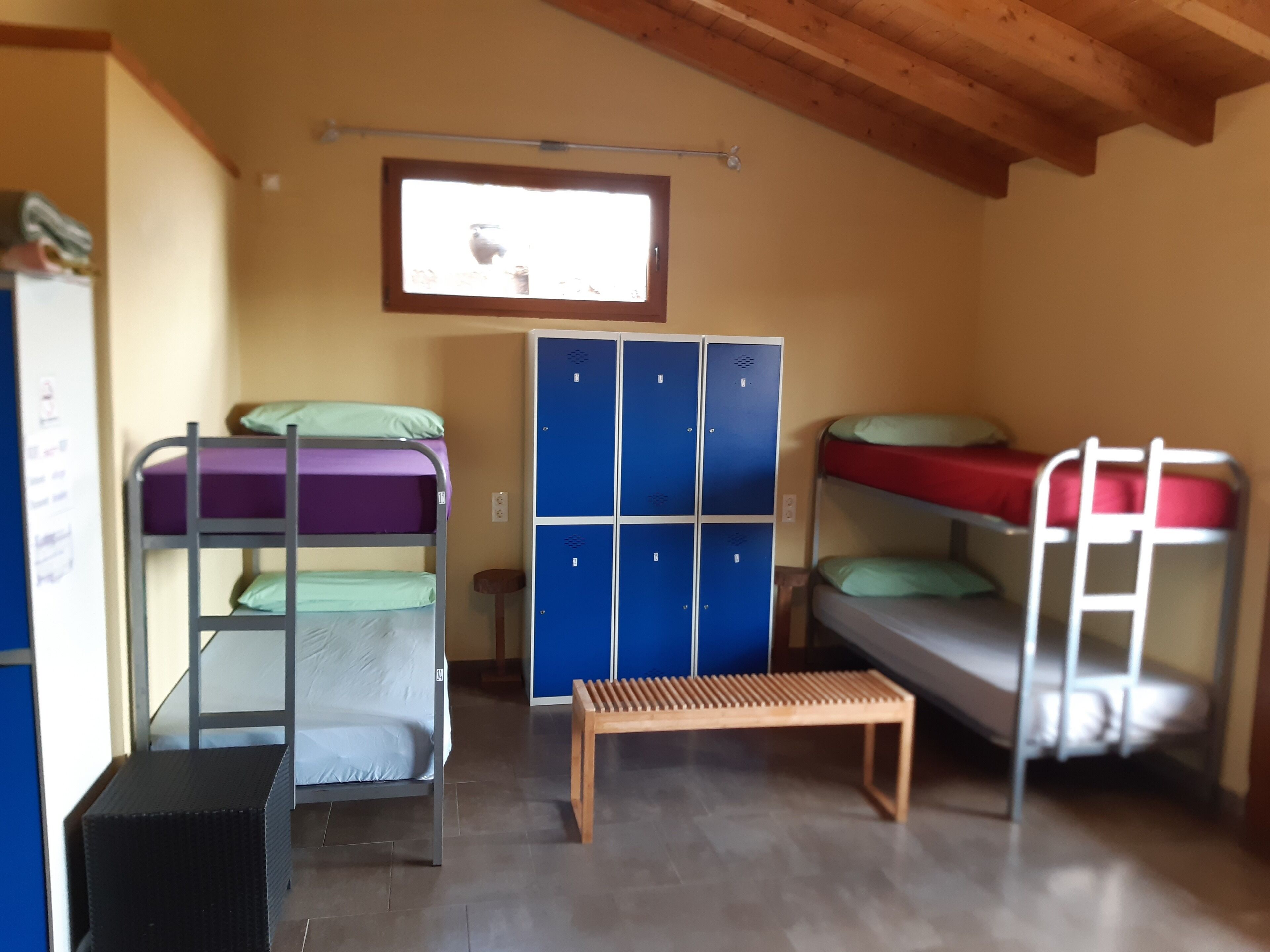 Un dormitorio con literas, un banco de madera y casilleros azules.