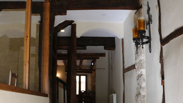 Un corridoio stretto con pareti in pietra, travi di legno e pavimento piastrellato.