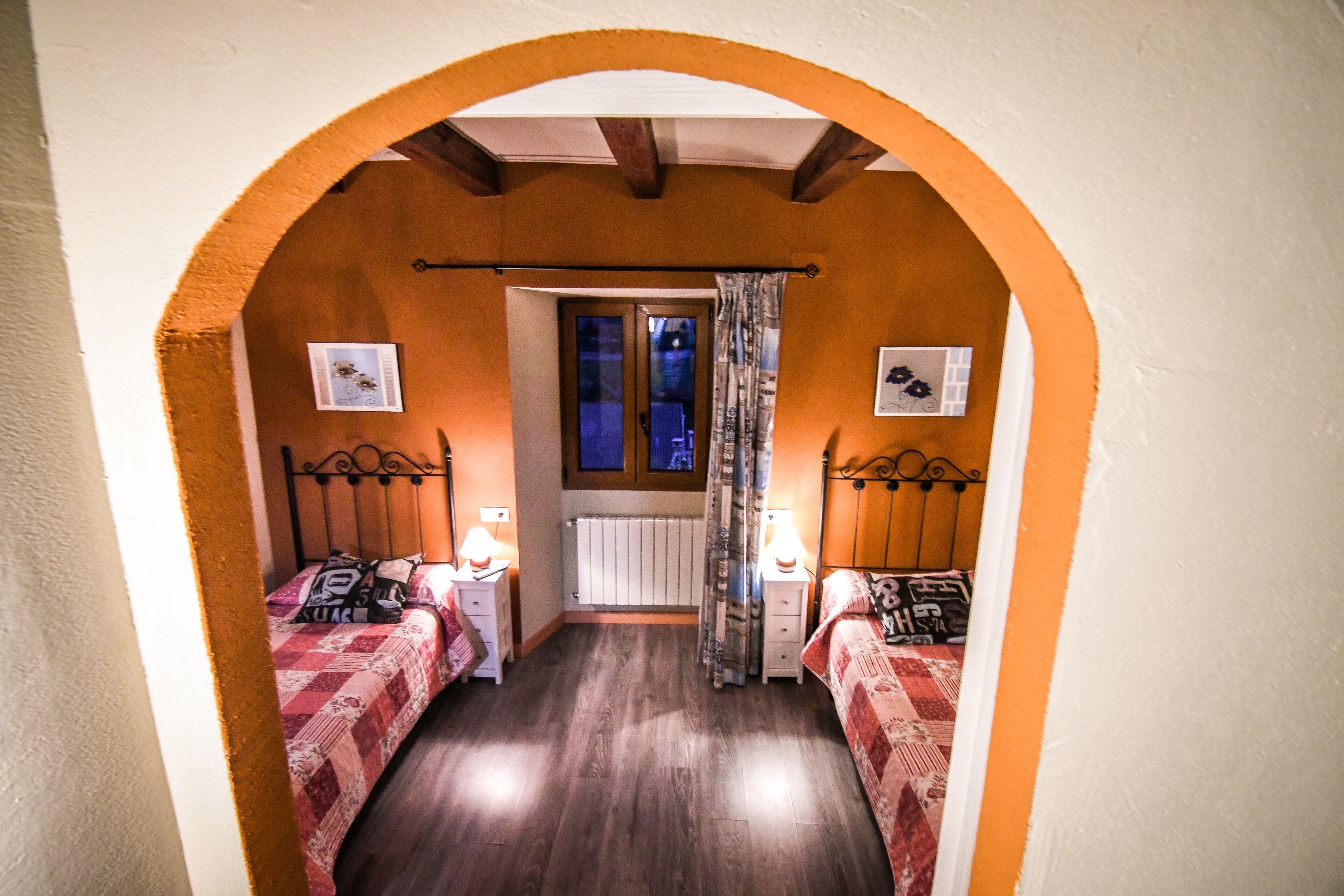 Un dormitorio con dos camas, una ventana con cortinas, un radiador y suelo de madera.