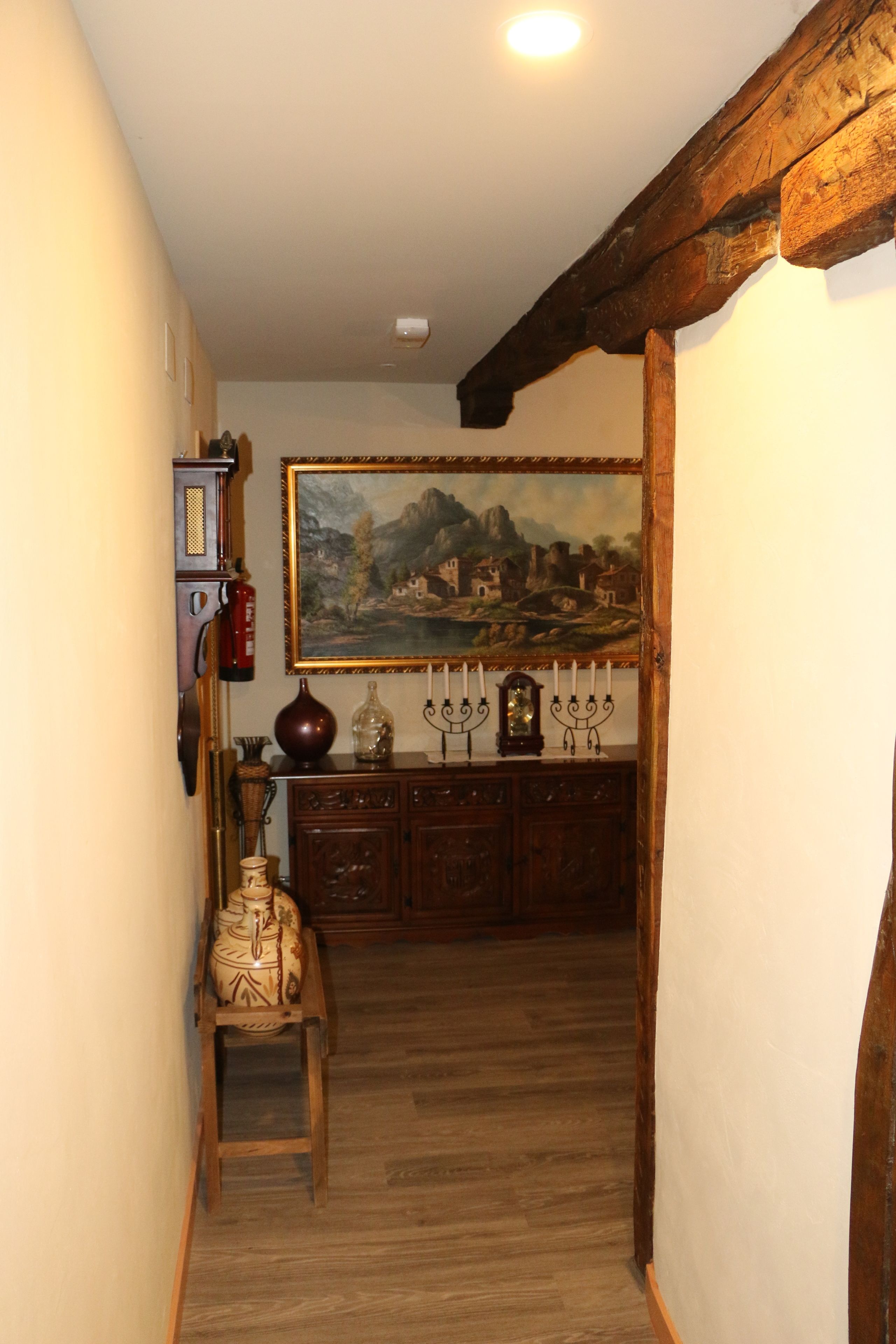 Passadís amb bigues de fusta, un quadre a la paret, un armari de fusta i una taula petita amb un ram.