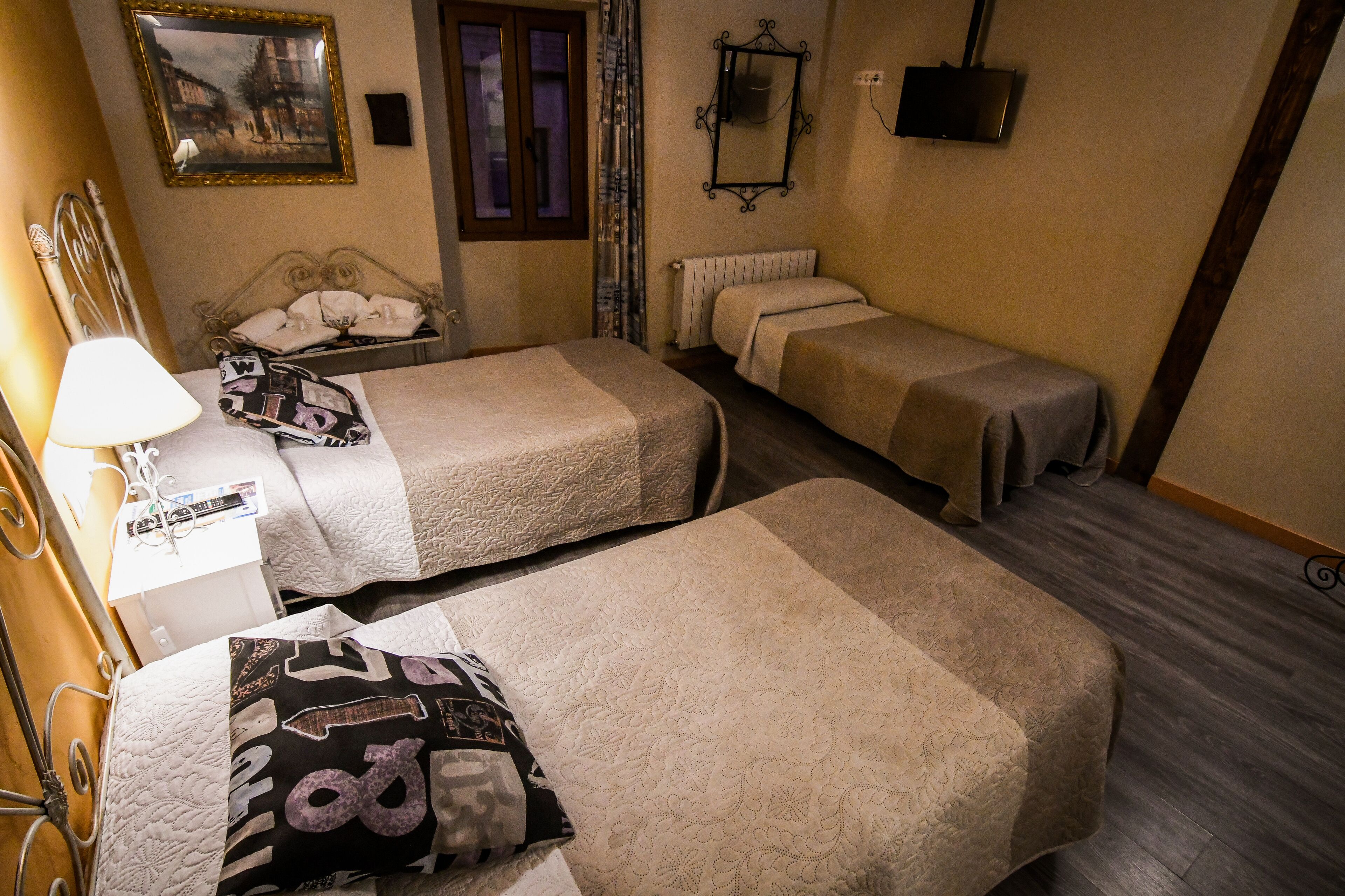 A hotel room with two single beds, a bedside table with a lamp, a framed picture on the wall, and a radiator.