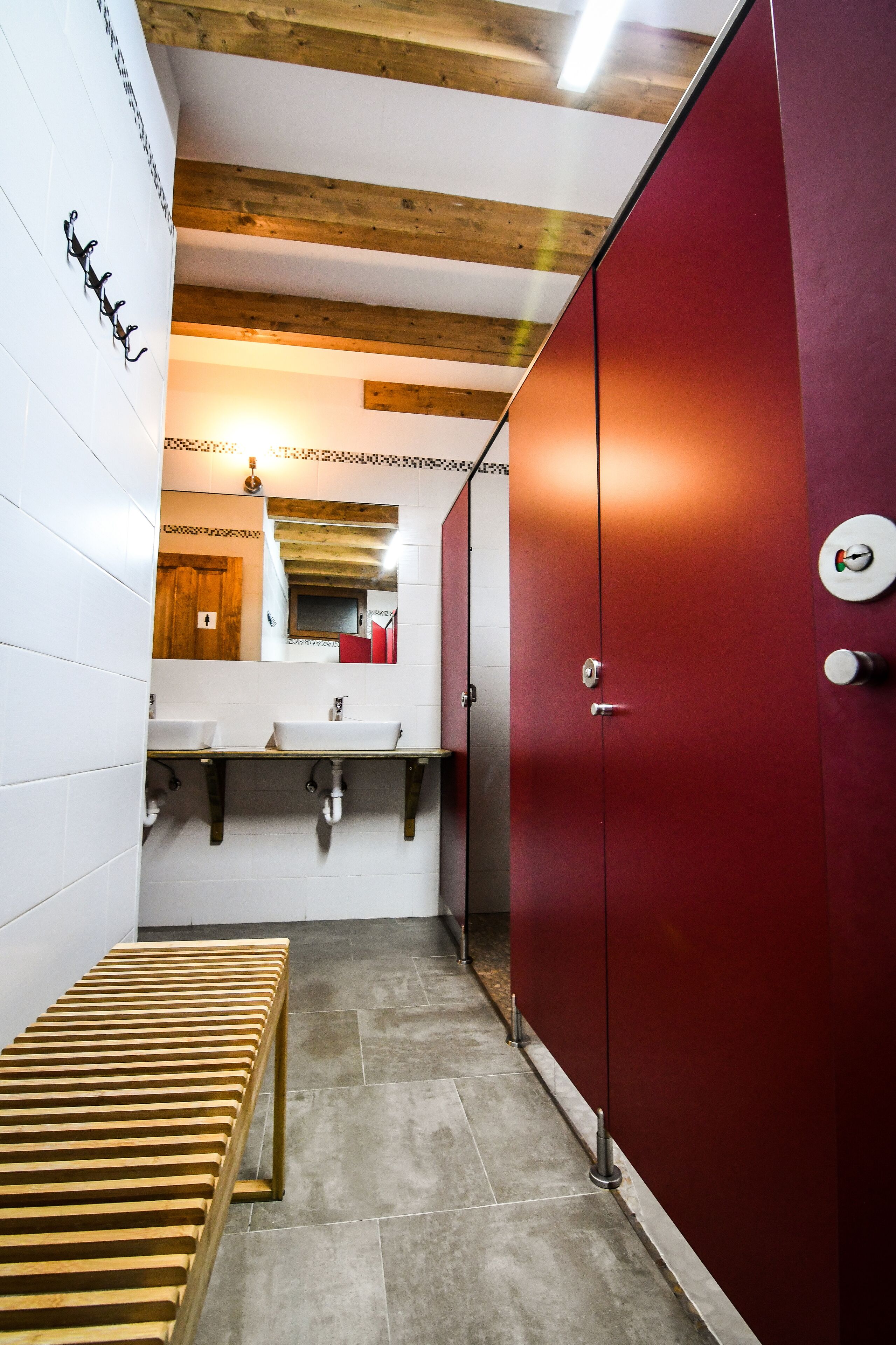 Un pasillo estrecho con un banco de madera, un armario rojo y un espejo que refleja un techo de madera y una puerta roja.