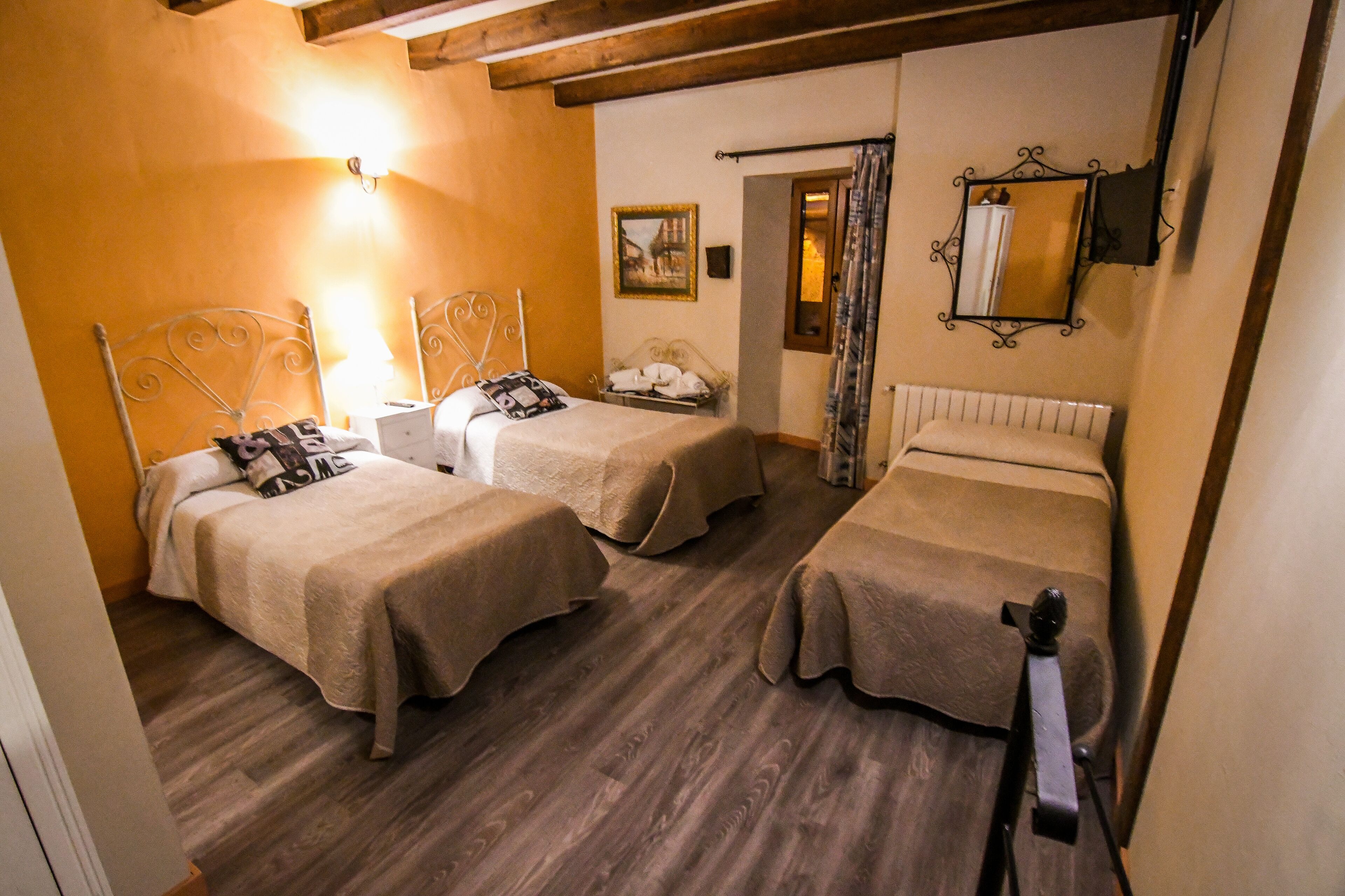 A room with two beds, wooden flooring, a painting on the wall, and a mirror.
