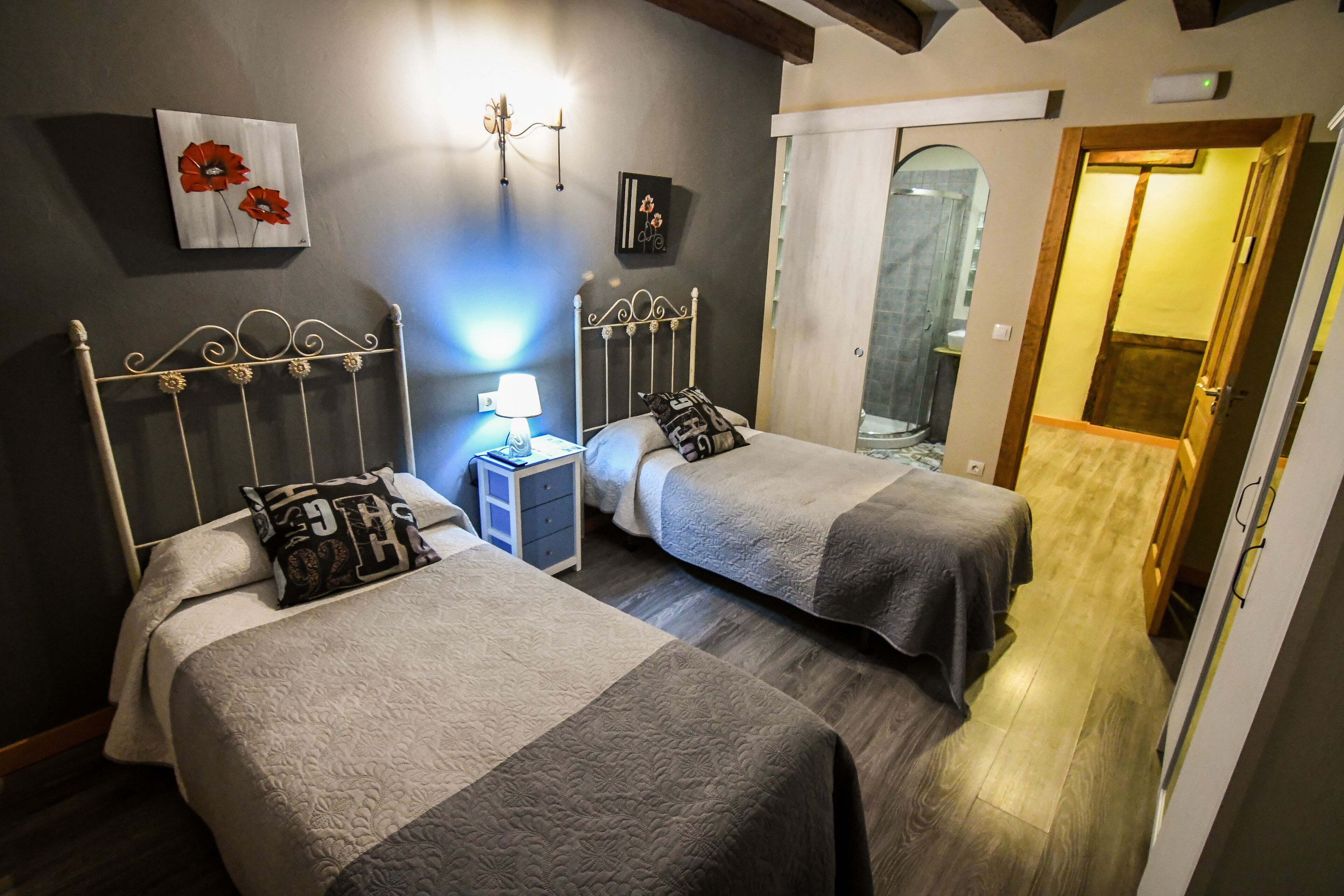 A bedroom with two beds, a nightstand, a lamp, and artwork on the wall.
