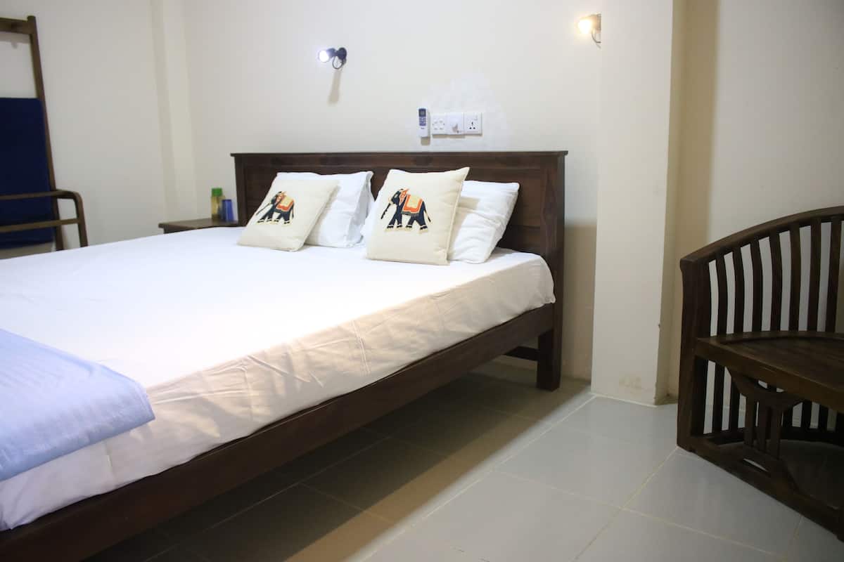 A neatly made bed with white linens and two decorative pillows, a wooden nightstand with a lamp, and a wooden chair.