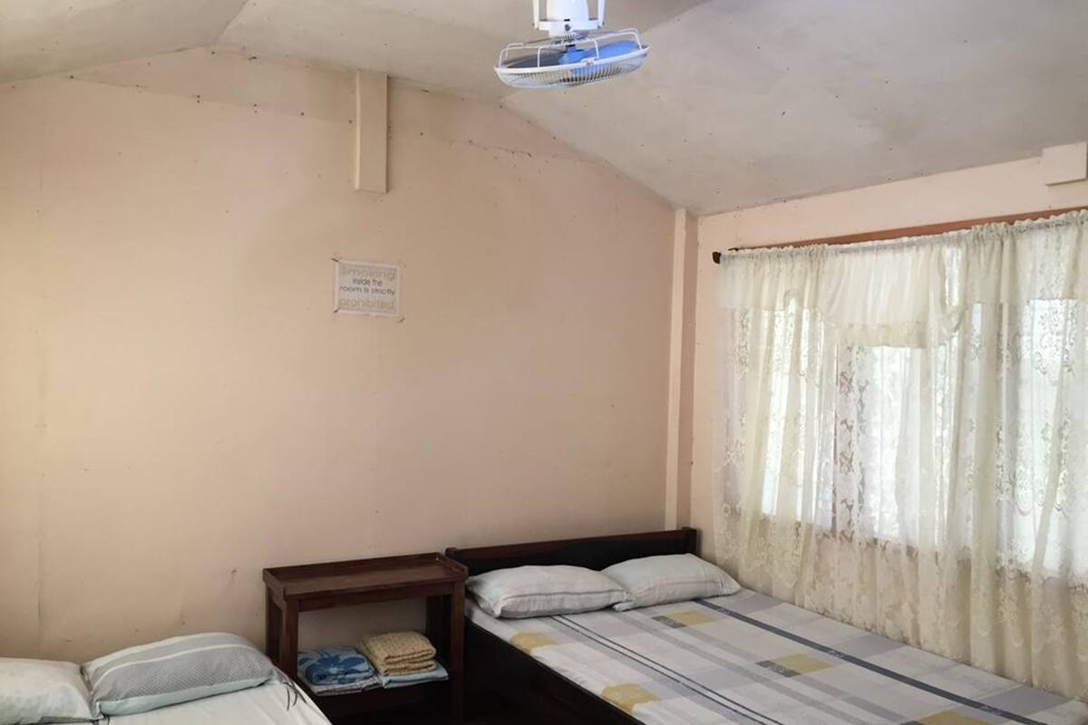 A small, simple room with two single beds, a small table, and a window with curtains.