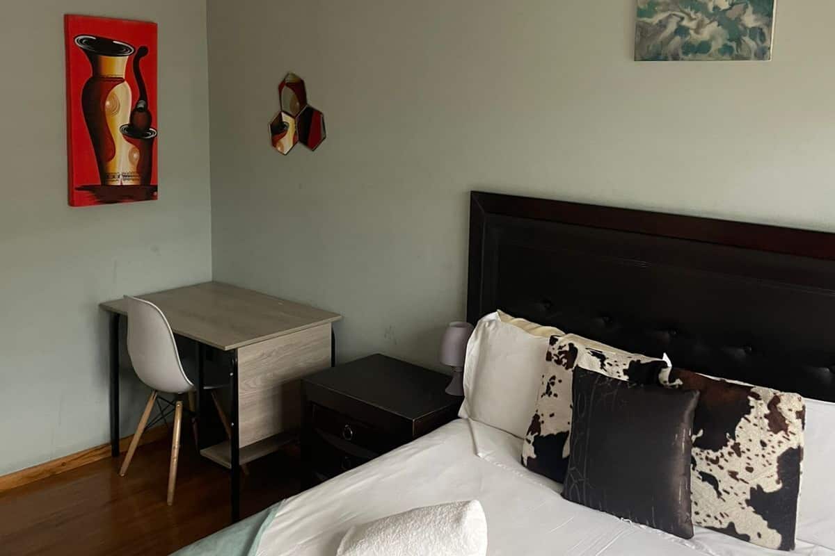 Une chambre d’hôtel avec un lit, un bureau et une chaise. Il y a deux tableaux accrochés au mur.