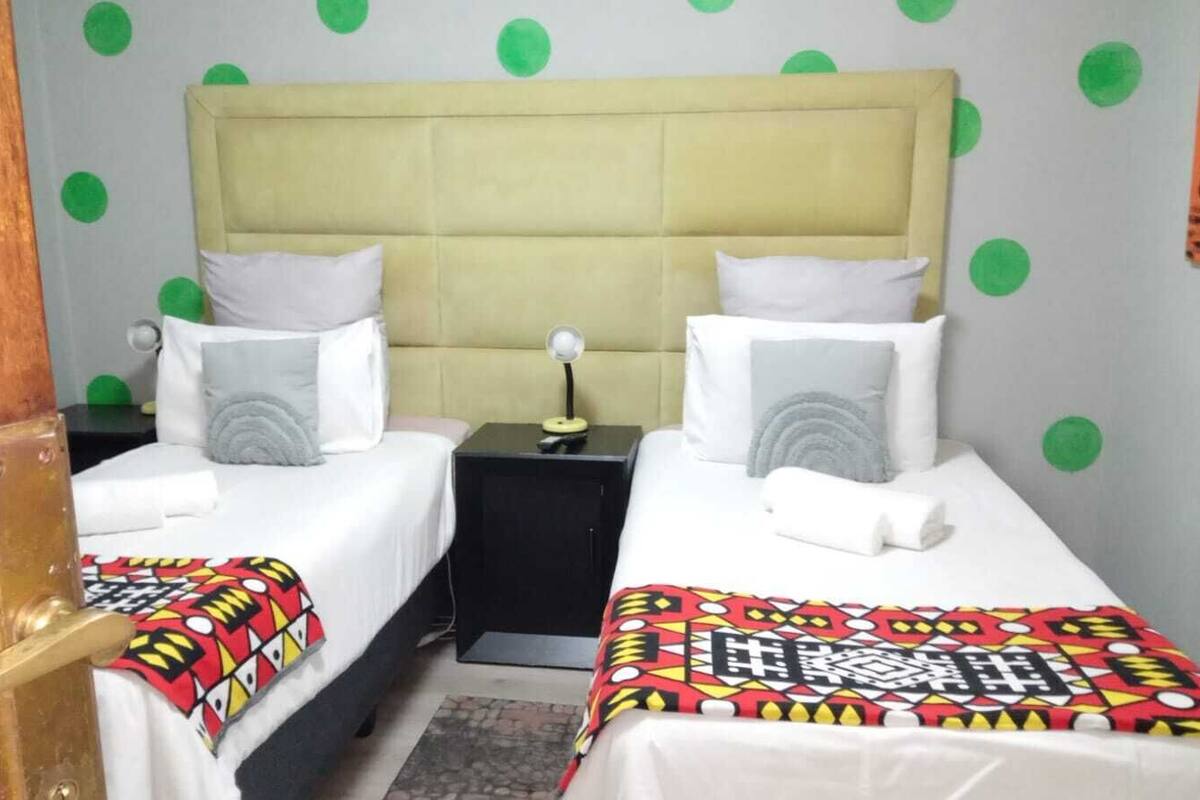 Une chambre d’hôtel avec deux lits simples, une table de chevet, une lampe et une porte dotée d’une poignée en laiton.