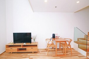Una sala moderna con televisor de pantalla plana sobre un mueble de madera, una mesa de comedor con sillas y una escalera con barandillas de vidrio.