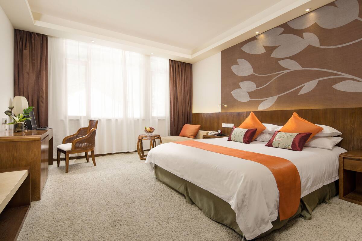 Una habitación de hotel con una cama grande, un escritorio, una silla y una mesita de noche con una lámpara.