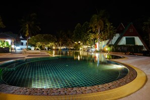 A swimming pool with a tiled edge, surrounded by palm trees and a building with a red roof.