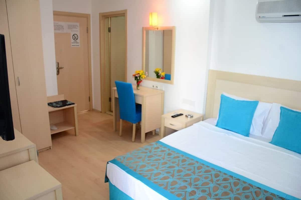 A hotel room with a bed, a desk, a chair, a wardrobe, and a mirror.