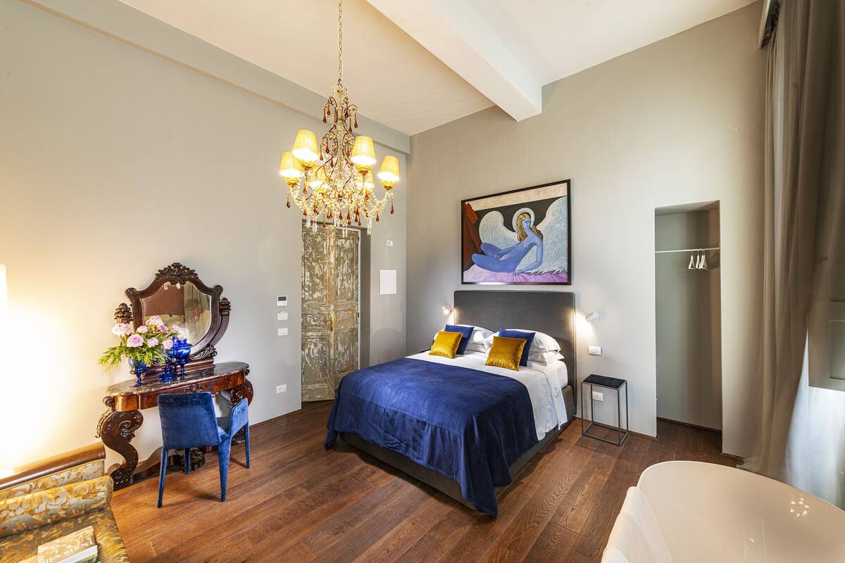 Un dormitorio con una cama grande, un aparador, una silla, una araña y un cuadro en la pared.