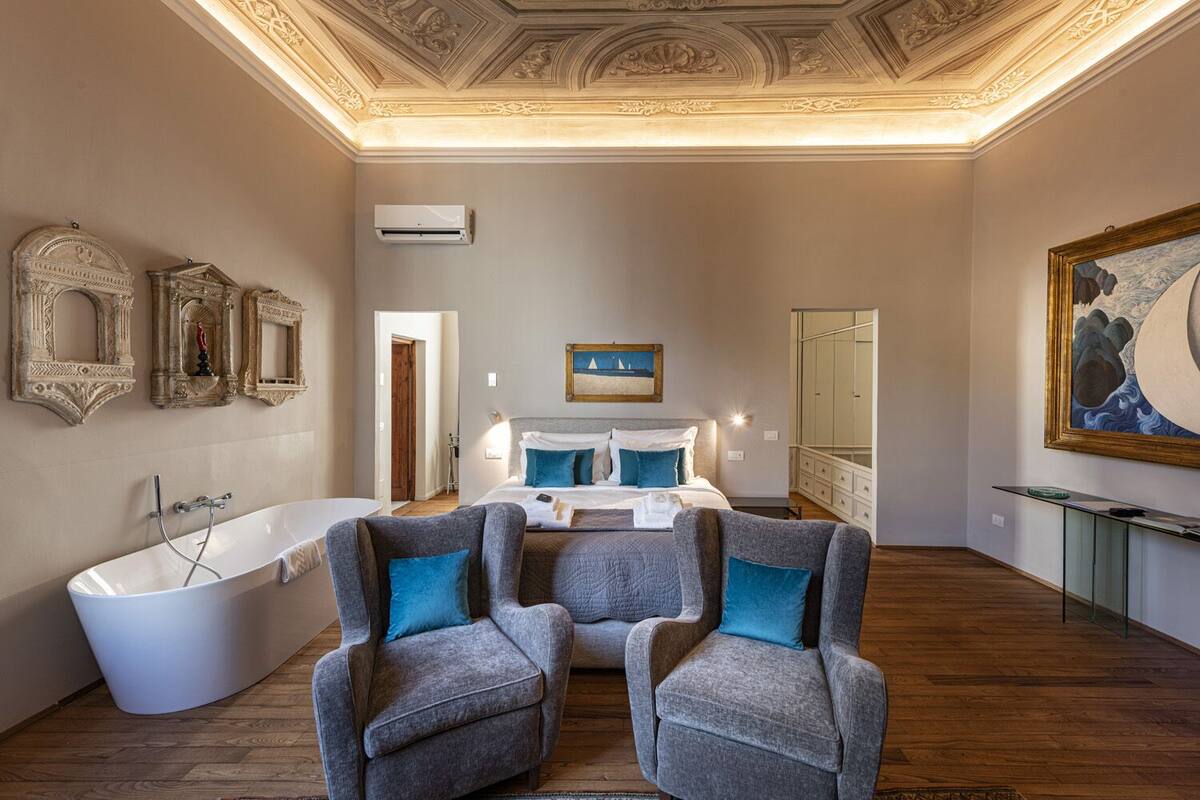 Un dormitorio con una cama grande, una bañera y dos sillones.