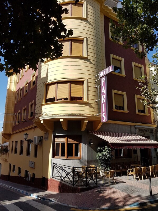 Un edificio en esquina con un letrero que dice 'HOTEL PARIS', que presenta una fachada curva, numerosas ventanas y un área de estar al aire libre.