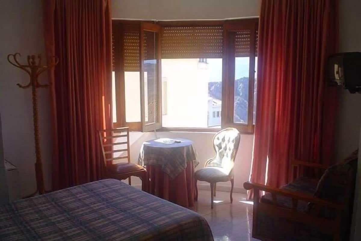 A room with a bed, a small table, two chairs, and a window with curtains.