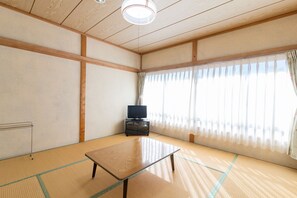 A tatami mat room with a television on a cabinet, a tatami mat table, and a window with sheer curtains. - Chokiya (Fujikawaguchiko)