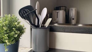 Cozinha com suporte cinza para utensílios, contendo uma planta, um batedor e diversos utensílios brancos e pretos.